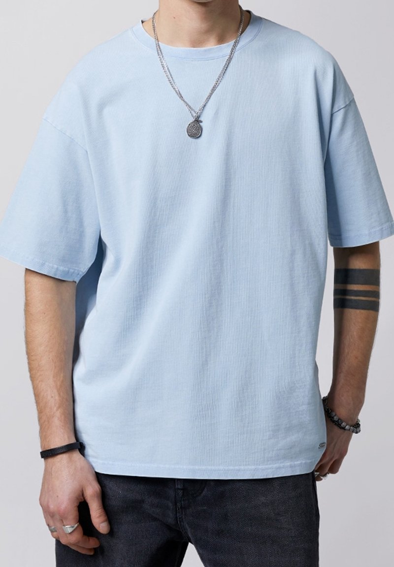 Lyseblå bomulds-t-shirt med afslappet pasform, korte ærmer, rund halsudskæring og ribbet tekstur. Båret med sølvhalskæder og armbånd.