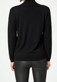 Svart stickad tröja med hög krage och ribbat mönster. Har långa ärmar och en lös passform som faller nedanför höfterna.