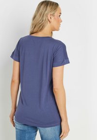 Fioletowy T-shirt krótki rękawek z okrągłym dekoltem i podwiniętymi mankietami, wykonany z miękkiego materiału. Posiada luzny krój i zaokrąglony dół.