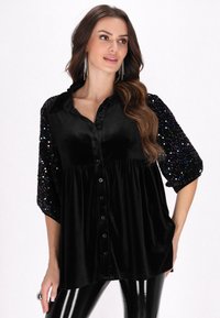 Black velvet blouse with sequined sleeves, featuring a button-down front and a flowing silhouette. Smooth texture and glossy finish.