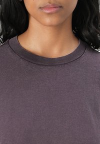T-shirt a girocollo di colore viola scuro, realizzato in tessuto testurizzato, con maniche corte e un design semplice e classico senza ulteriori decorazioni.