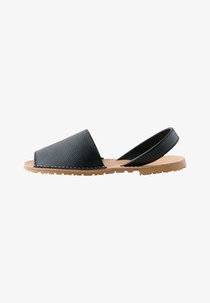Schwarze offene flache Sandale mit strukturiertem Lederobermaterial und Riemen hinten auf einer hellbraunen Gummisohle mit Ziernähten.