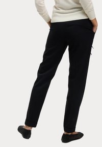 Svarta tapered byxor med subtil struktur, sidofickor och manschett, i kombination med svarta vävda slip-on skor.
