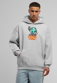 Grå oversized hettegenser med frontlomme og ribbestrikket kant, med et fargerikt grafisk trykk av kloden og "market studios" i oransje.