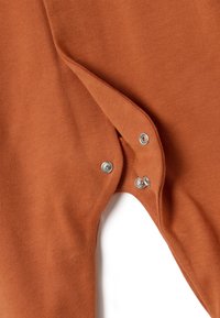 Tela de prenda de color óxido con textura suave, que presenta cierres de presión bordeados en plata a un lado para un fácil abrochado.