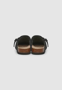 Sabots en feutre noir avec une semelle en liège et une semelle en caoutchouc, dotés d'une sangle ajustable et d'une texture douce. La vue arrière montre des talons ouverts et une forme arrondie.