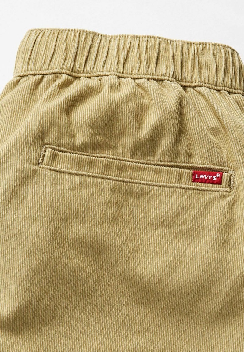 Bermudas de pana beige con una superficie texturizada, que cuentan con una cintura elástica y un bolsillo trasero con una etiqueta roja de Levi's.