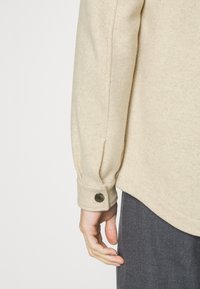 Beige fleece shirt met een knoopmanschette en een zachte, gestructureerde afwerking, gecombineerd met donkere broeken.