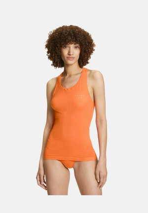 Kvinde med krøllet hår iført en tætsiddende orange tanktop og matchende undertøj, stående foran en ensfarvet hvid baggrund.