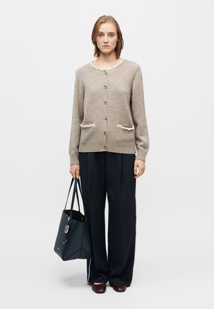 Cardigan en maille beige avec un col festonné, sept boutons, deux poches avant et des poignets côtelés, associé à un pantalon noir à jambes larges et un sac cabas bleu marine.