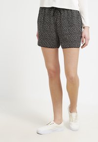 Shorts noirs avec un motif en points blancs, ceinture élastique avec un cordon de serrage et coupe décontractée. Associés à des baskets blanches.