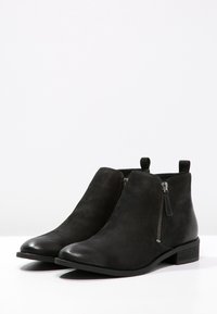 Bottines en suede noir avec un bout rond, des zips sur le côté et un petit talon empilé, dotées d'une languette à l'arrière pour un enfilage facile.