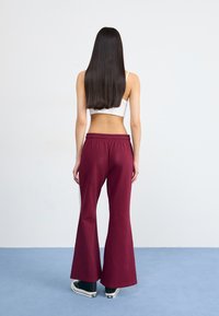 Bordeauxfarvede flare sweatpants med elastisk talje, parret med sorte høj-top sko. Teksturen er blød, velegnet til afslappet brug.