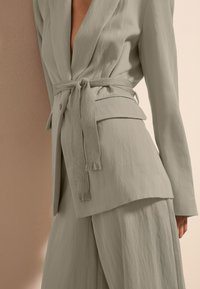 Lichtgrijze blazer met riem en een gestructureerde afwerking, heeft een diepe V-hals en een gestroomlijnd ontwerp met bijpassende brede pantalons.