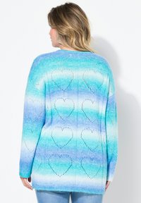Cardigan in maglia grossa con sfumature gradienti di blu e teal, caratterizzato da motivi a cuore e un taglio morbido. Tessuto soffice, maniche lunghe.
