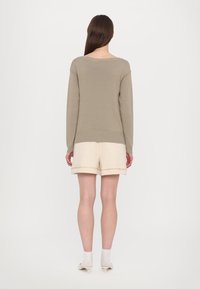 Lys beige strikket genser med bred hals, parret med kremfargede shorts med brettet kant og subtil teksturdetalj.