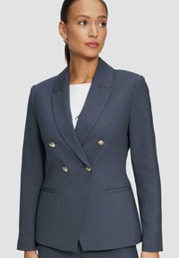 Blazer double boutonné bleu marine avec boutons dorés, revers à cran, poches latérales et coupe ajustée. Tissu texturé avec un motif subtil.