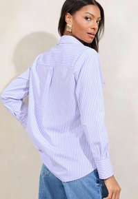 Camicia a maniche lunghe, viola chiaro con righe verticali bianche, colletto classico, dettaglio con piega sul retro, polsini con bottoni, abbinata a jeans a vita alta.