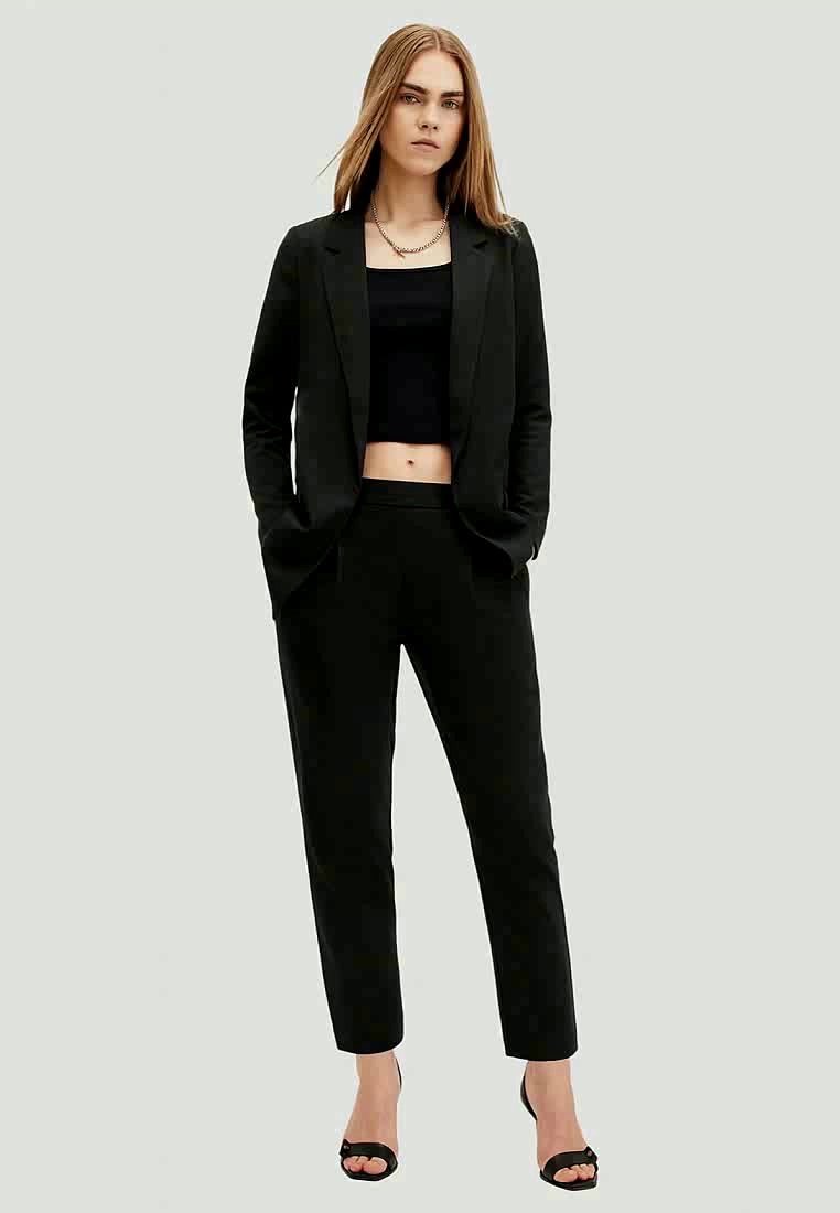 Blazer noir ajusté sur un crop top noir, associé à un pantalon noir structuré. Tissu lisse, coupe slim, avec de subtils poches avant.