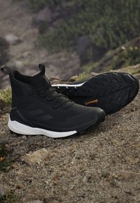 Black hiking shoes with a textured upper, reinforced toe, and pull tabs. The white midsole contrasts with the rugged black outsole.