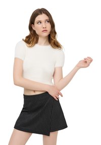 Cropped top bianco e peloso a maniche corte con scollatura rotonda abbinato a una mini gonna avvolgente nera a righe.