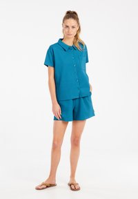 Tamsiai mėlyna trumpomis rankovėmis marškinėliai su kišenėle krūtinėje, derinami su atitinkamais šortais. Lygus paviršius, laisvas kirpimas ir kasdieniai šlepetės.