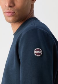 Felpa blu navy con un patch rotondo del logo Colmar sulla manica sinistra, con scollo a giro e tessuto texture.
