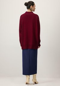 Pull oversize bordeaux, texture tricotée, manches longues et col, associé à une jupe bleu marine et des bottines stilettos couleur crème.