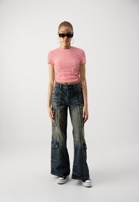Rød og hvit stripete kortermet crop top, kombinert med mørke vide cargo-jeans med lommer og et slitt preg. Svarte solbriller på.