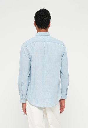 Camicia in chambray azzurro chiaro con maniche lunghe, polsini abbottonati e piega posteriore. Presenta un colletto classico e un orlo curvo.