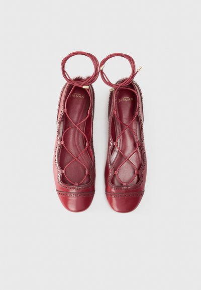 Maroon leather ballet flats with lace-up design, decorative perforations, and a smooth finish. Features a rounded toe and flat sole.