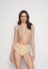 Naadloze nude beha met dunne bandjes, een gladde textuur en een diepe uitsnijding. Hoge taille nude slip met naadloze randen, beide gemaakt van rekbare stof.