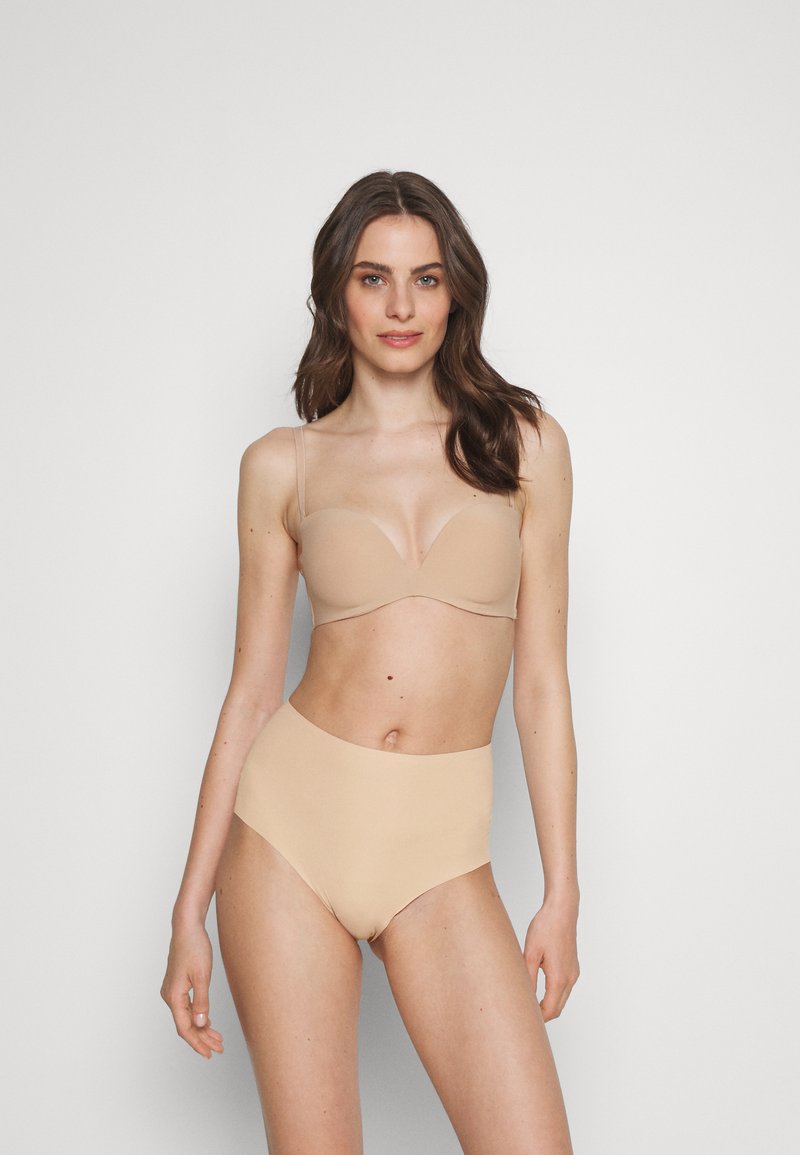 Naadloze nude beha met dunne bandjes, een gladde textuur en een diepe uitsnijding. Hoge taille nude slip met naadloze randen, beide gemaakt van rekbare stof.