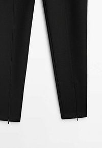 Pantalons noirs en matériau lisse, présentant un design ajusté, des zippers latéraux à l'ourlet et des coutures soignées le long des coutures.