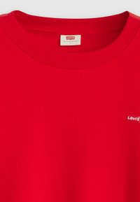 Red cotton t-shirt with a round neckline and short sleeves. Features a small white Levi's logo on the left chest. Smooth texture.