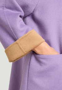 Lila wollen jas met een beige manchet, voorzien van een zachte textuur en een zijzak. Het manchet heeft een duidelijk contrasterende kleur en materiaal.
