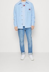 Ljusblå fleecejacka med knapp-up framsidan, bröstficka och kontrasterande logotyp. Kombineras med ljusblå jeans och vita sneakers.