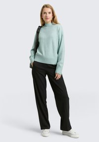 Jasnoniebieski sweter dzianinowy z wysokim kołnierzem, zestawiony z czarnymi szerokimi spodniami i białymi trampkami, na jednolitym tle.