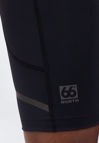 Gros plan sur un short de sport noir avec des coutures visibles, une bande réfléchissante et un logo "66° NORTH" sur la jambe.