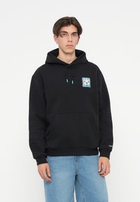 Sweatshirt preto feito de tecido suave, com um bolso frontal. Apresenta um emblema gráfico no peito e detalhes em turquesa nos cordões e punhos.