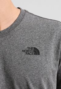 Šedé bavlněné tričko s kulatým výstřihem. Obsahuje malé černé logo "The North Face" na oblasti levého hrudníku. Jemná textura.