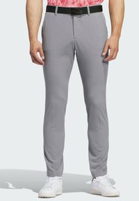 Pantalones gris claro con un acabado suave, diseño ajustado, frente plano y cinturón negro. Combinados con zapatillas blancas.