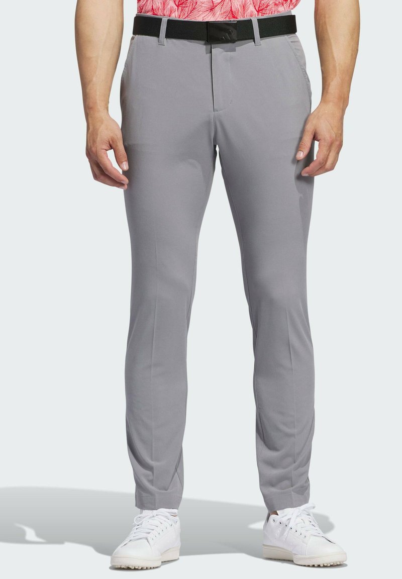 Pantalones gris claro con un acabado suave, diseño ajustado, frente plano y cinturón negro. Combinados con zapatillas blancas.
