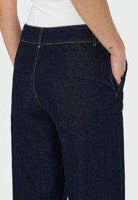 Mörka jeans med en åtsittande midja, sidofickor och detaljer i gyllene sömmar. Slät textur med en klassisk passform.