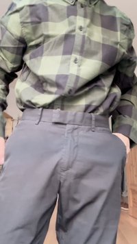 Camicia a maniche lunghe a quadri verdi e neri con chiusura a bottoni, abbinata a pantaloni grigi scuri, caratterizzati da una superficie liscia e una vestibilità standard.