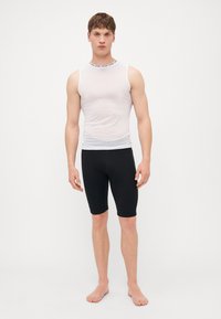 Haut sans manches blanc avec un motif texturé et une bande noire autour du col ; associé à un short noir moulant s'étendant jusqu'à mi-cuisse.