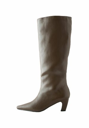 Spetsig tå knähög stövel i mjukt taupe läder med en slät yta. Har en måttlig blockklack och en figursydd överdel.