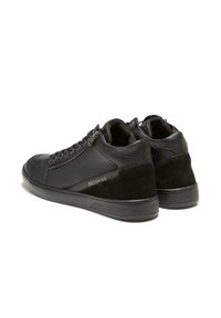 Baskets montantes noires en cuir et daim, avec des lacets, une fermeture éclair sur le côté et une semelle en caoutchouc texturé, arborant le logo "REDSKINS".