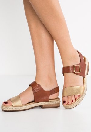 Sandales en cuir marron et doré avec une semelle de style espadrille, dotées d'une bride à boucle et d'un design à bout ouvert. Texture lisse avec un talon plat.