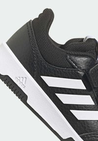 Černá sportovní bota s texturovaným koženým svrškem, síťovinovými detaily, bílými akcenty a třemi charakteristickými pruhy po straně. Gumová podešev.